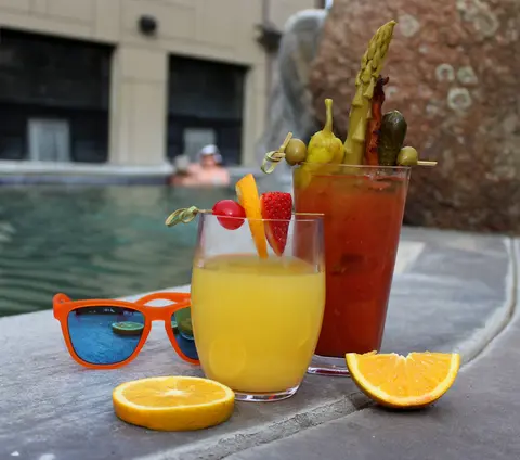 Two cocktails and sunglasses sit poolside.