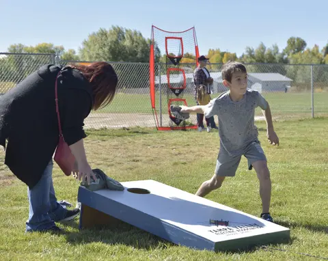 A boy and a woman play cornhole outdoors on a grassy field.