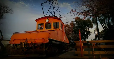 A bright orange vintage electric locomotive stands on tracks outdoors.