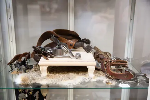 A display case features vintage spurs with leather straps resting on a small wooden stand and fur rug.
