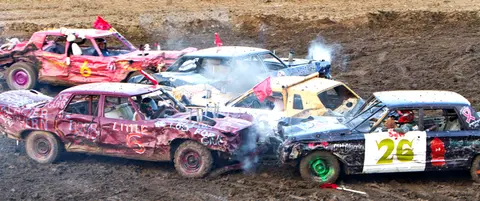 A demolition derby with multiple wrecked cars in a dirt arena.