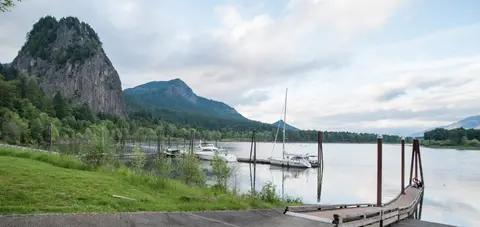 A river dock with boats and a large rock formation in the background.