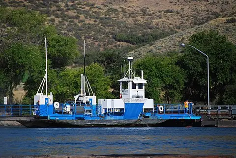 A blue and white ferry boat on the water with hills in the background.