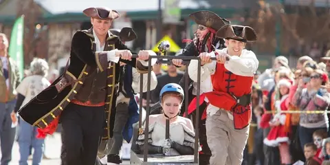 People dressed as pirates participate in a parade, pushing a cart with a person sitting in it.