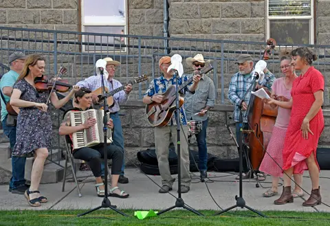 A band playing music outdoors with a string bass, accordion, guitars, and a fiddle.