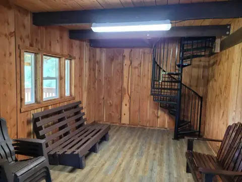 An interior view of a wooden room with a spiral staircase, benches, and windows.