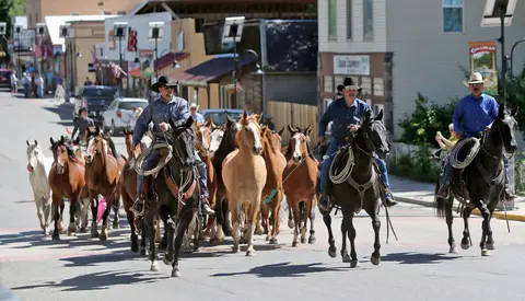 Cowboys ride horses down a street.