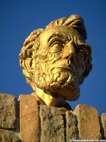 A close-up view of a golden bust mounted on a stone wall against a blue sky.