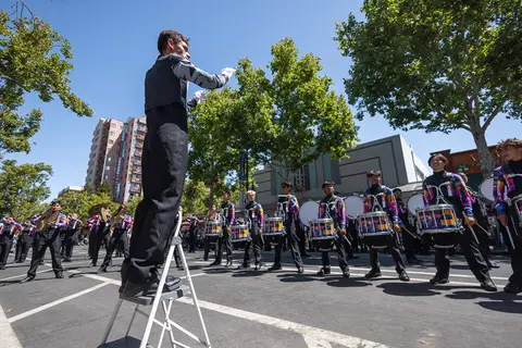 A marching band with a conductor standing on a stepladder performing on a city street.