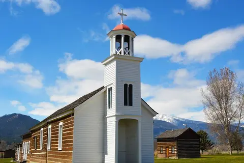 A historic wooden church with a bell tower under a partly cloudy blue sky.