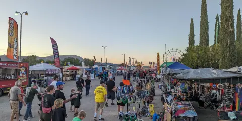 A crowd of people walking through an outdoor street market with vendor stalls and food trucks.