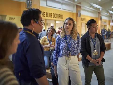 A group of people wearing lanyards stand inside a building.