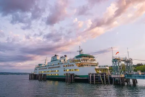 A large ferry is docked at a pier during sunset.