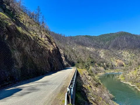 A narrow mountain road running alongside a river and rocky slopes.