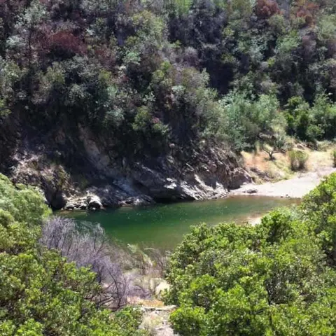A river pool surrounded by wooded hills and rocks.