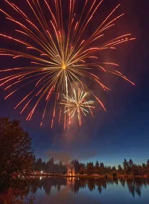 A large firework explodes over a lake at night.