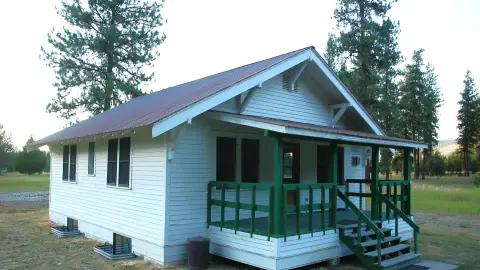 An exterior view of a small white house with a green porch railing and trim.