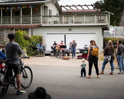 A small band performs in front of a house for a crowd of people.