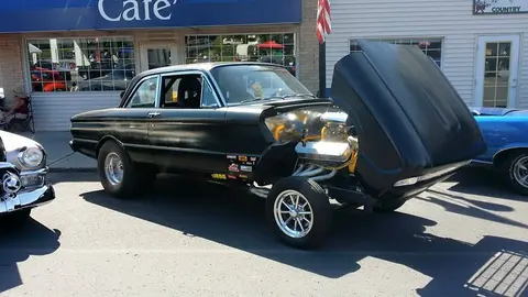 A classic black car is parked outside with its hood open.