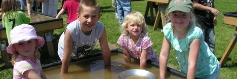 Four children pan for gold in a trough outdoors.