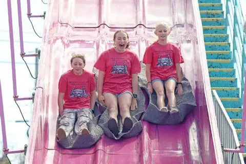 Three girls ride down a large slide at an amusement park.