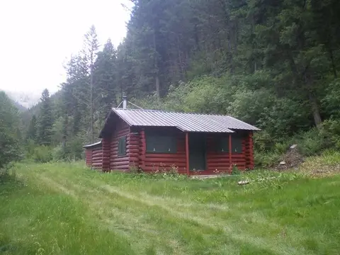 A rustic log cabin sits in a clearing near a forest.
