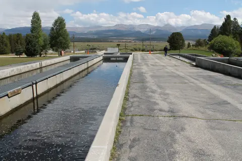 An outdoor fish hatchery featuring concrete raceways with mountains in the background.