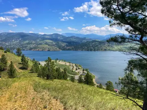 A scenic view of a large lake surrounded by rolling hills and mountains under a blue sky with clouds.
