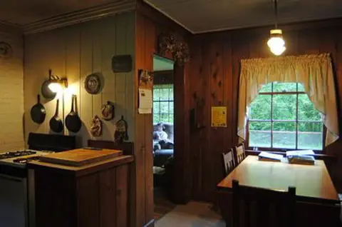 An interior view of a rustic kitchen and dining area with wooden walls and hanging cookware.