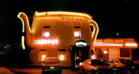 A brightly lit building shaped like a large coffee pot at night.
