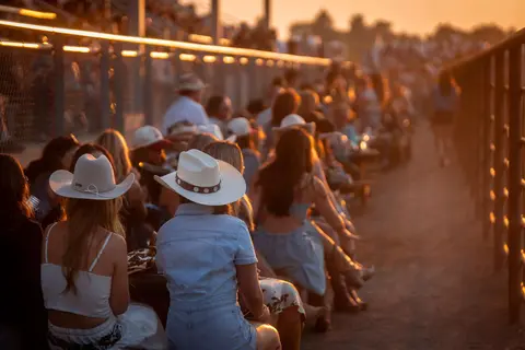 A crowd of people wearing cowboy hats sits at an outdoor event during sunset.