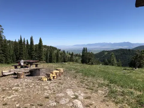 A scenic view from a mountain overlook showing a picnic table, fire ring, and distant mountains.