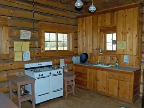 The inside of a log cabin kitchen featuring a white stove and wooden cabinets.
