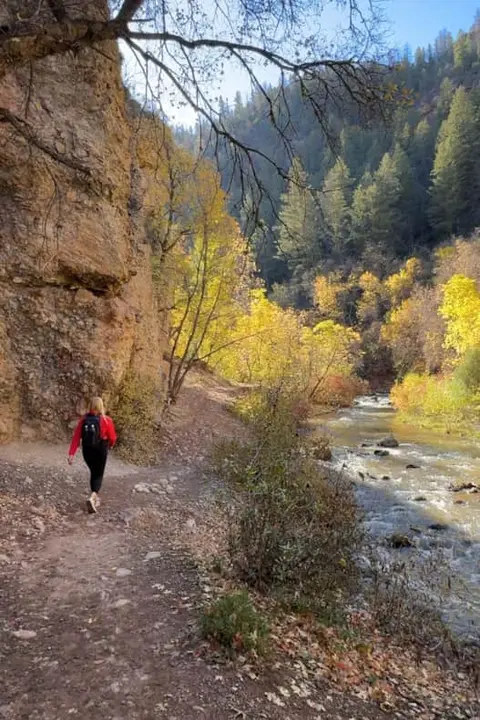 A person hikes on a trail beside a river with autumn foliage.