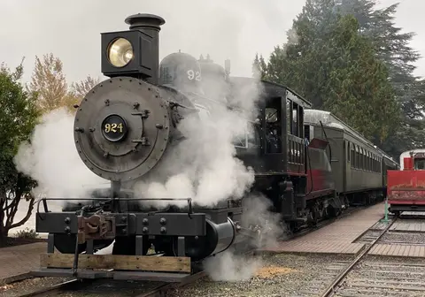 A steam locomotive emits smoke while stopped at a station platform.
