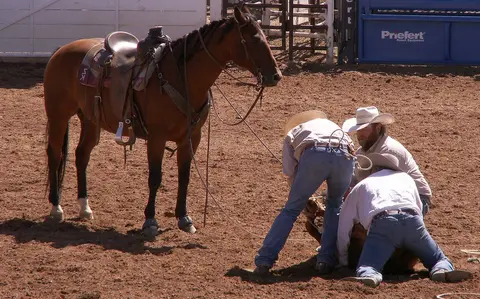Three people and a saddled horse in a rodeo arena.