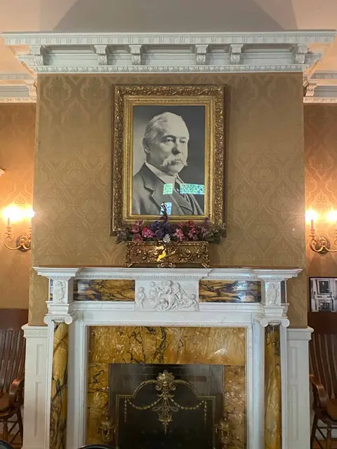 A framed portrait hangs above an ornate fireplace inside a room.