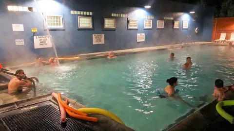 People relaxing in an outdoor hot spring pool at night.