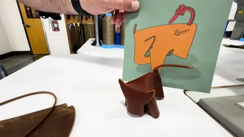 A person holds up a green card with an illustration next to a leather figurine on a table.