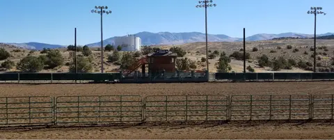 An empty dirt arena with fences and a small building under a clear blue sky.