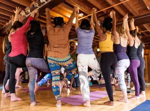 A group of people practicing yoga indoors with hands raised.