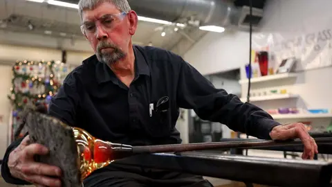 A man shapes hot glass in a workshop.