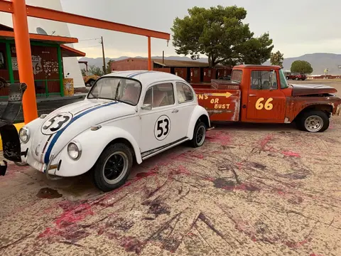 A white car with the number 53 and a rusty orange truck with the number 66 parked outside.