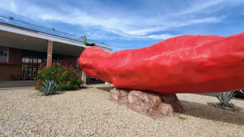 A large red chili pepper statue stands outside a building.