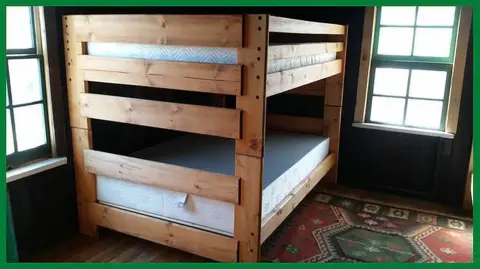 A custom wooden bunk bed sits inside a room with two windows and a patterned rug.