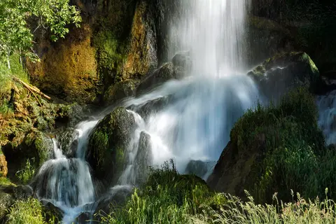 A waterfall cascades over mossy rocks and lush green vegetation.