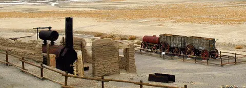An old abandoned boiler and wagons sitting in an arid landscape.