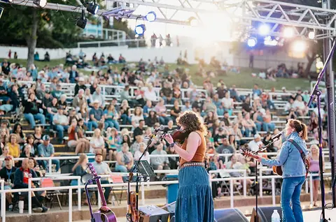 Musicians perform on a stage in front of a seated crowd outdoors.