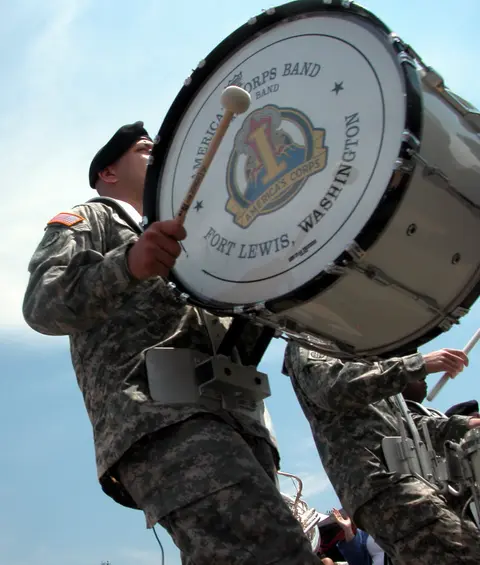 A soldier in uniform plays a large bass drum with a band logo.