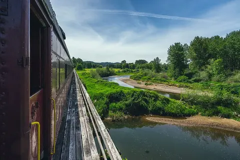 A view of a river and landscape from a train on a wooden bridge.